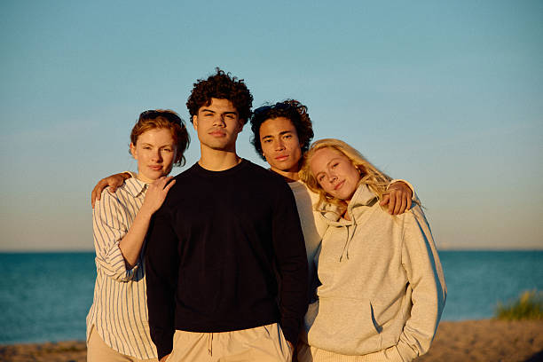 istock Four affectionate friends on beach with arms around each other looking at camera 2223044615