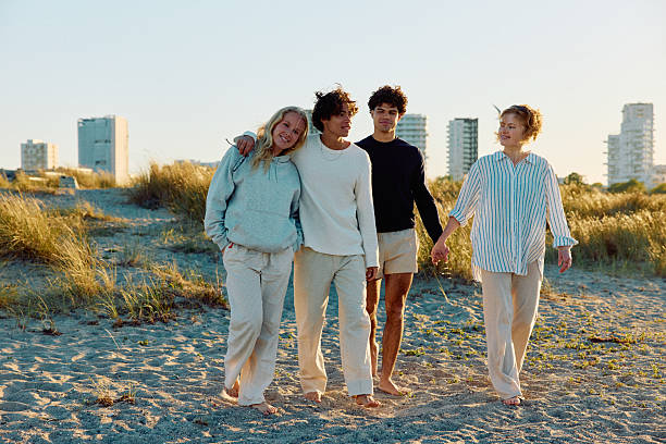 istock Four affectionate friends walking across beach, two holding hands, woman resting head on boyfriend's shoulder 2223044616