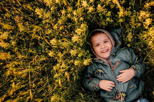 Peaceful portrait of a young boy lying on his back in a green meadow, surrounded by grass and nature. Calm and relaxed outdoor moment.
