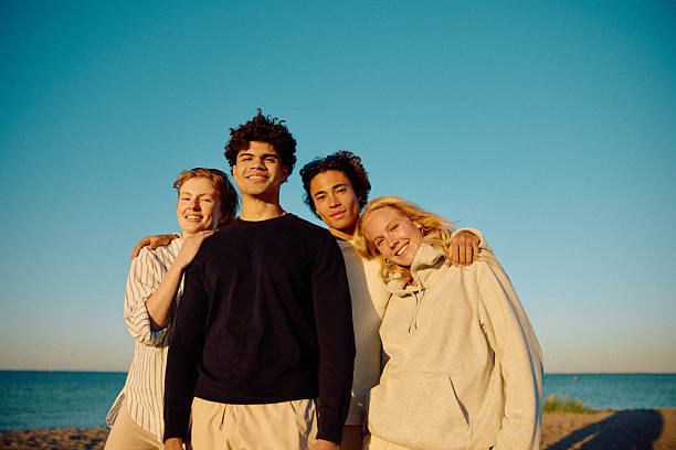 istock Four affectionate friends on beach with arms around each other smiling towards camera 2223044650