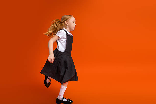 istock Active young schoolgirl in a uniform running on an orange background symbolizing a vibrant back-to-school theme 2223044749