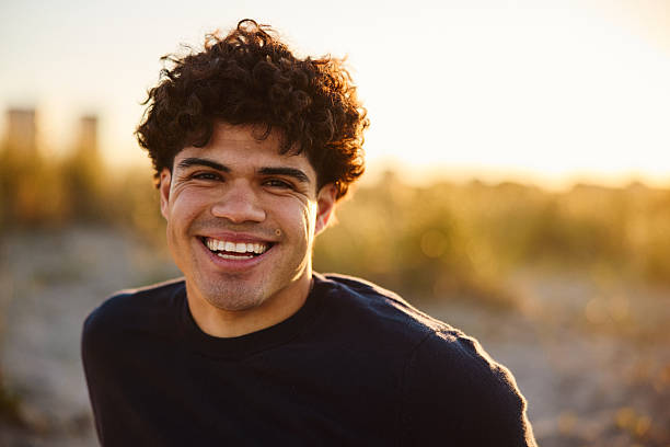 istock Happy young man sitting on a sandy beach and smiling at the camera at sunset 2223045079