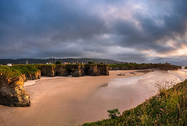Dramatic sky over As Catedrais beach Galicia Spain iconic rock arches towering above tidal sand at low tide green cliffs framing natural monument wonder strength timeless beauty