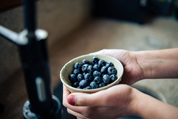 Young man eating healthy snack with blueberries and checking messages on smart phone in modern kitchen