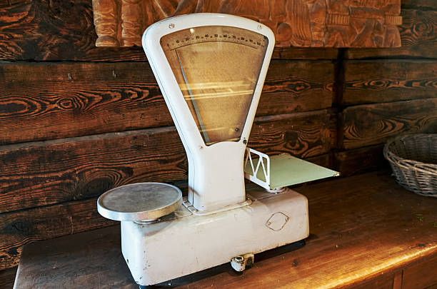 An old scale sits on a wooden table. The scale is white and has a black base. The scale is old and has a vintage look to it