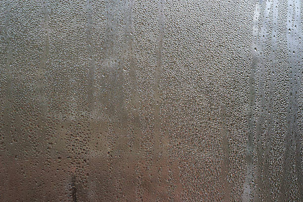 istock pattern of condensation forms on a chilled glass surface, with water droplets. abstract blurred background of wet glass. window of apartment were covered with drops from poor heating. 2223051220