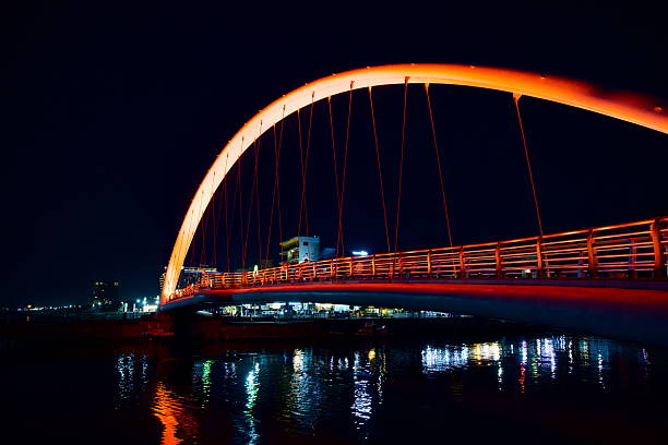 Gangneung, South Korea - May 31st 2025: The glowing red arc of Gangmun Sotdae Bridge casts colorful reflections onto the dark East Sea waters below, framing the quiet nighttime waterfront.