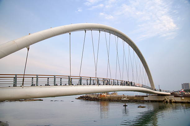 Gangneung, South Korea - May 31st 2025: A graceful white arch supports the Gangmun Sotdae Bridge, where walkers enjoy a seaside view over calm water near Gyeongpo and the East Sea coastline.