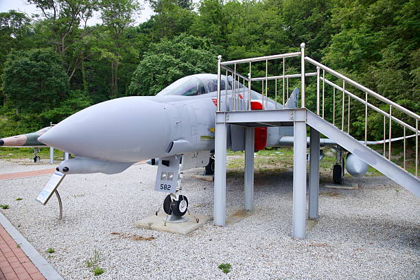 Gangneung, South Korea - June 1st 2025: A decommissioned fighter jet sits on display with access stairs, surrounded by gravel and forest, at Gangneung Unification Park.