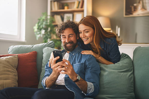 istock Happy couple relaxing on sofa and browsing internet on smartphone at home 2223065221