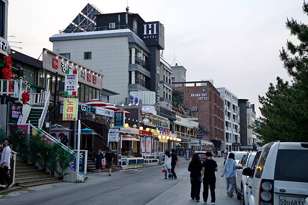 Gangneung, South Korea - May 31st 2025: Evening pedestrians pass seafood eateries, convenience stores, and boutique hotels along the road just behind Gyeongpodae Beach's shoreline.