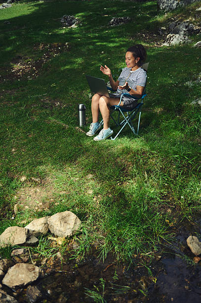 Woman Relaxing Outdoors Using a Laptop in a Natural Setting by a Calm Stream