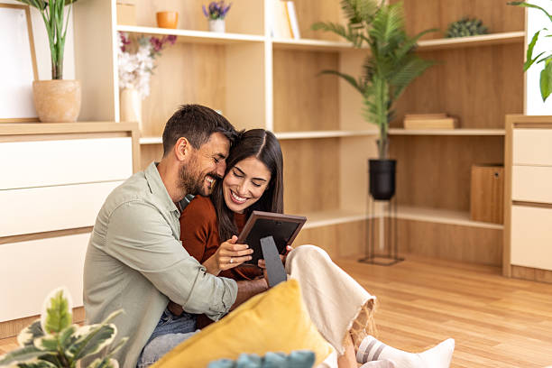istock Happy couple smiling and embracing while looking at photo frame at home 2223070107