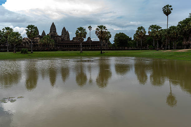 Angkor Wat, Cambodia – September 1, 2019: The towers of Angkor Wat and nearby palm trees are reflected in a calm pond after rainfall. This view of the historic temple highlights its iconic silhouette and tropical surroundings.