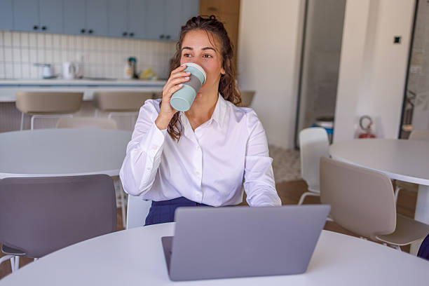 istock Businesswoman drinking coffee while working on laptop in office break room 2223072013