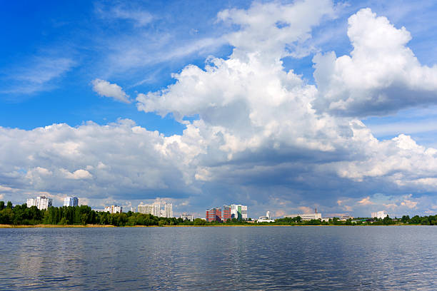 Wide-angle shot of urban skyline with buildings reflected in the lake, featuring dramatic clouds and clear blue skies.