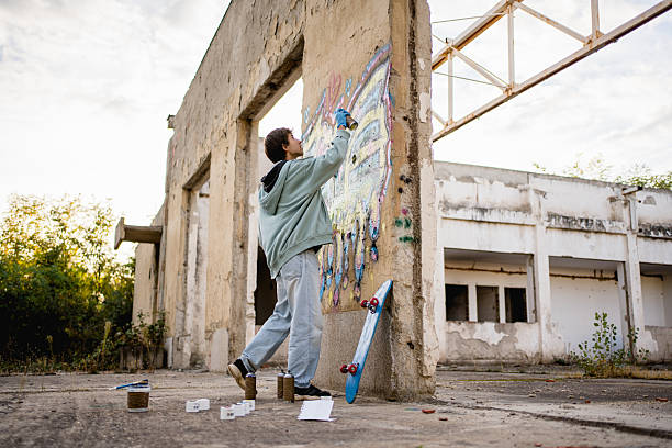 Young artist spray painting graffiti on abandoned building wall