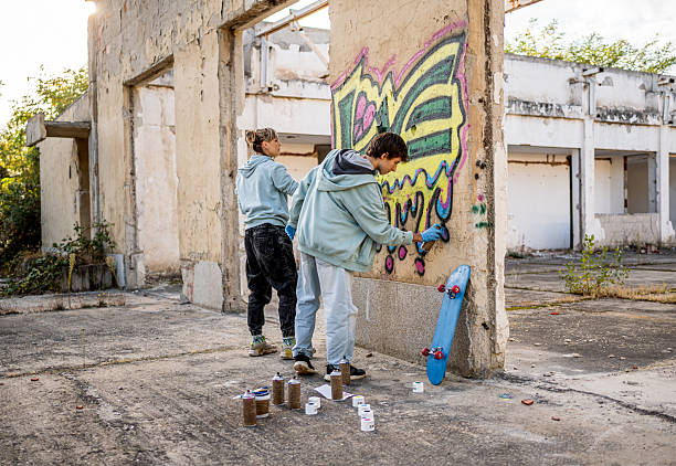 istock Two young graffiti artists spray painting on a wall in abandoned building 2223077187