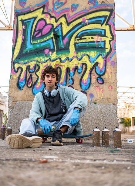 istock Young graffiti artist sitting on skateboard with spray cans 2223077414
