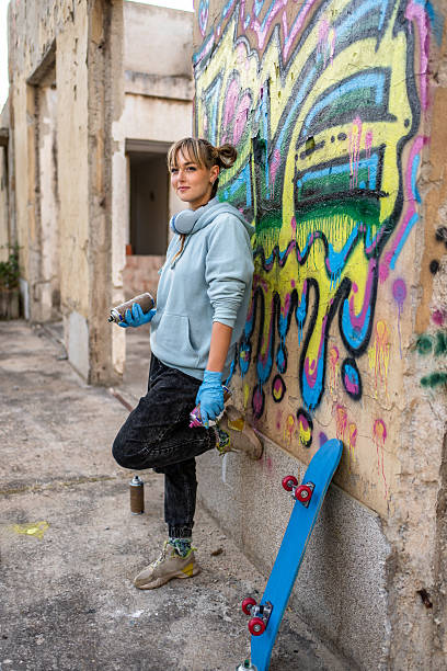 istock Young female graffiti artist posing with spray cans and skateboard 2223077533