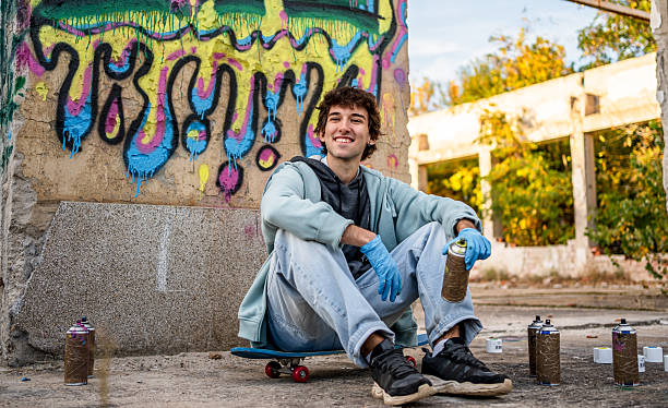 istock Young male graffiti artist sitting on skateboard by wall 2223077621