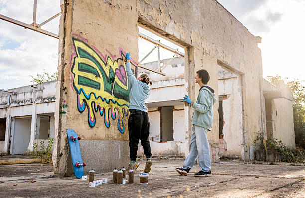 istock Two young graffiti artists spray painting on a wall in abandoned building 2223077651