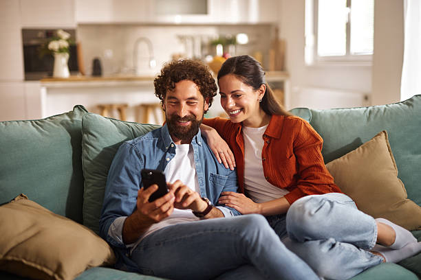 istock Happy couple relaxing on sofa browsing smartphone at home 2223080392