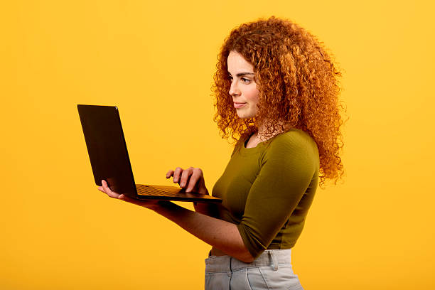 istock Redhead woman using laptop on yellow background 2223084009