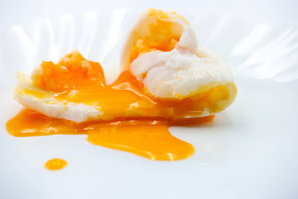 A poached egg sits on a clean white plate, with the white surrounding a vibrant yellow yolk that is oozing out. The presentation highlights the smooth texture and freshness of the egg.