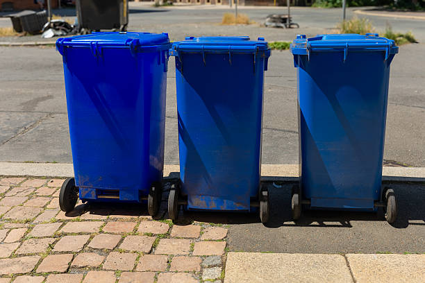 istock Bright blue trash bins lined up on cobblestone pavement under clear skies on a sunny afternoon in a quiet urban neighborhood 2223089507