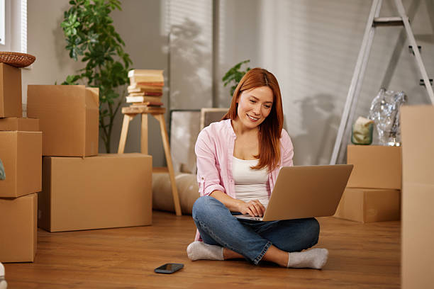 istock Woman using laptop while moving into new apartment 2223090257