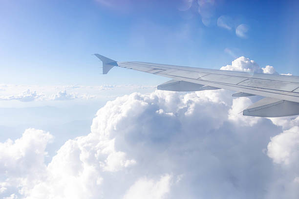 istock Airplane wing above fluffy white clouds with bright blue sky and sunlight shining through 2223091254
