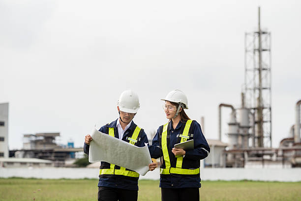 istock Two Engineers Collaborating on a Blueprint During a Site Walk at a Factory. Two people wearing safety gear and holding papers 2223093279