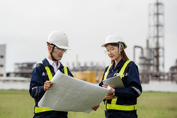 istock Engineering Team Analyzing Blueprint and Tablet Data at an Industrial Site. Two people wearing safety gear and holding papers 2223093282