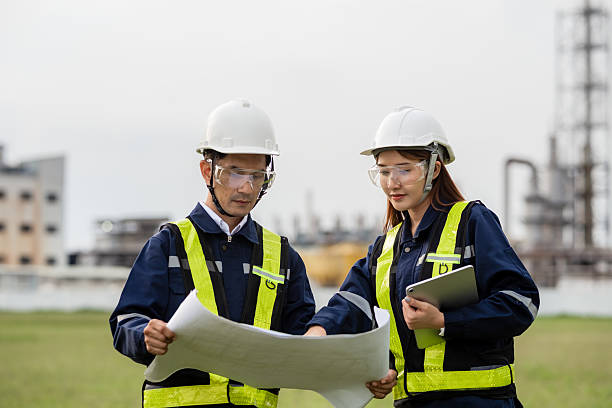 istock Engineering Team Analyzing Blueprint and Tablet Data at an Industrial Site. Two people wearing safety gear and holding papers 2223093286