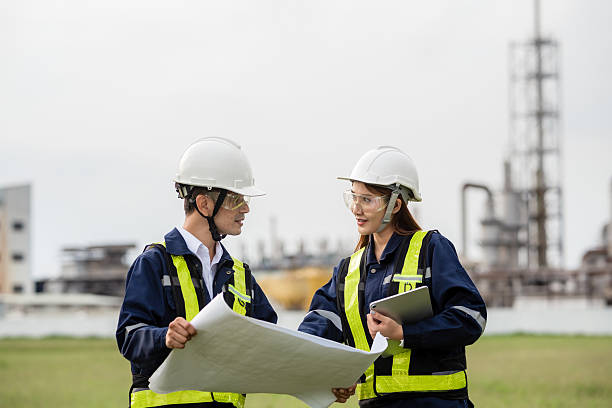 istock Two Engineers Happily Discussing a Project Plan with a Blueprint and Tablet. Two people wearing safety gear and holding papers 2223093289