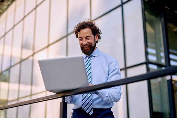 istock Smiling businessman using laptop in front of office building 2223103347