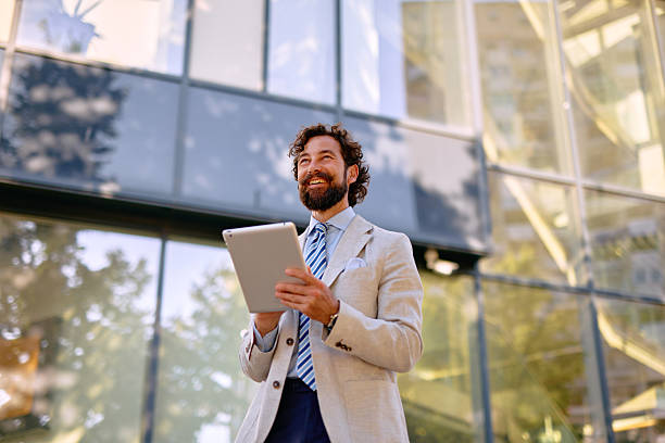 istock Businessman smiling and using digital tablet in front of modern office building 2223103419