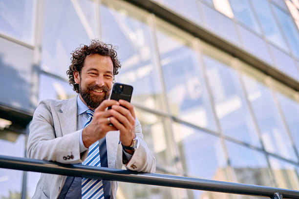 istock Smiling Businessman Using Smartphone in front of Office Building 2223103467