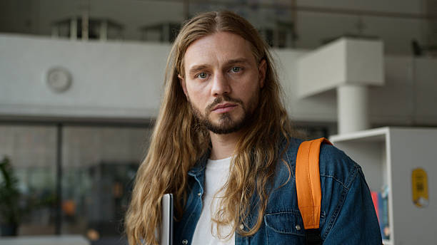 istock Dreaming pensive serious calm thoughtful man male guy student think looking in corridor look at camera holding laptop portrait in university college education studying learning learn study course 2223120927