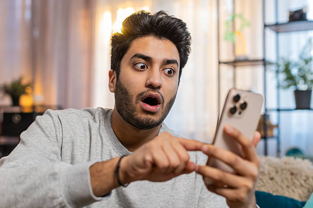 istock Happy man using smartphone scrolls through news on smartphone reacting with surprise and excitement 2223121847