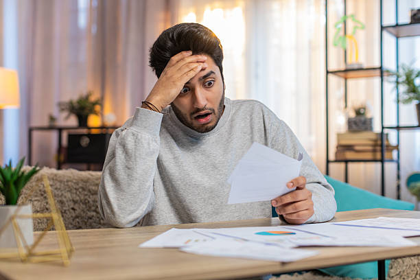 istock Young Indian man frustrated with bills and expenses while reviewing documents at home on table 2223121871