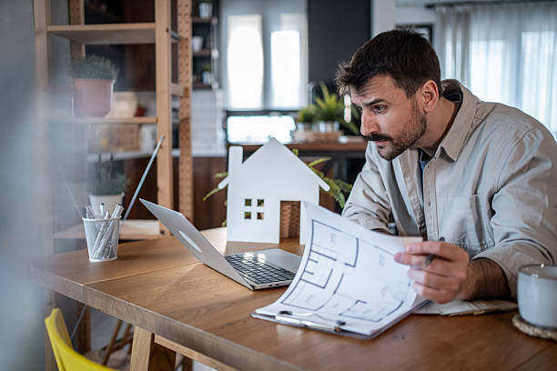 istock Architect reviewing blueprints and working on laptop in home office 2223122925
