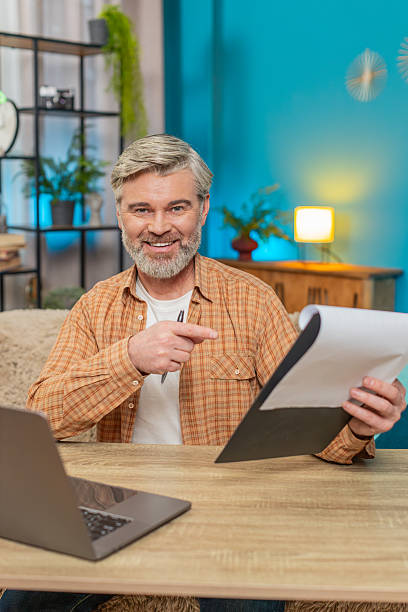 istock Mature man sitting on table with documents and laptop, smiling from successful work at home office 2223128324