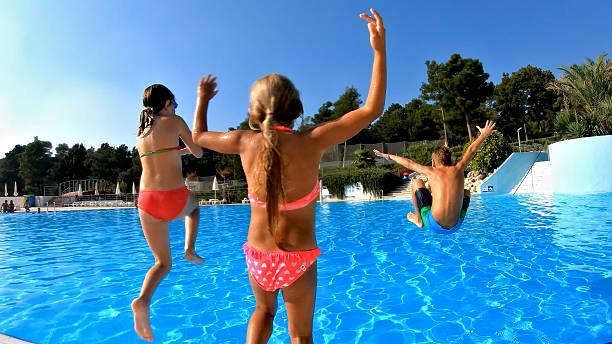 Cheerful group of three relaxed females friends having fun in outdoor swimming pool under the sun. Vacation and freedom, summer vibes concept