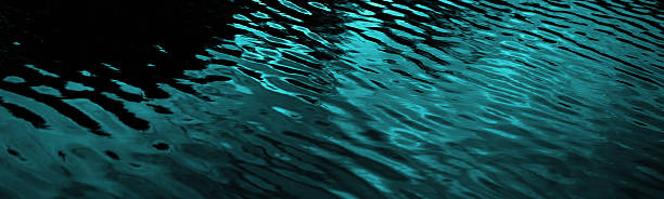 Black dark blue green teal water. Night. Ripples reflection light moonlight. Little waves. Gradient. Abstract. Contrast. Sea surface. Background with space for design. Wide banner. Panoramic.