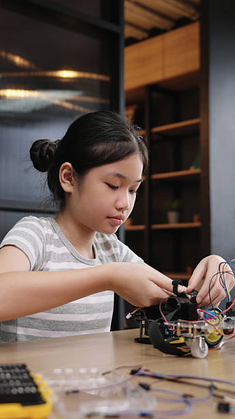 Asian girl student concentrates on assembling robotics project in classroom, showing science learning and focus.
