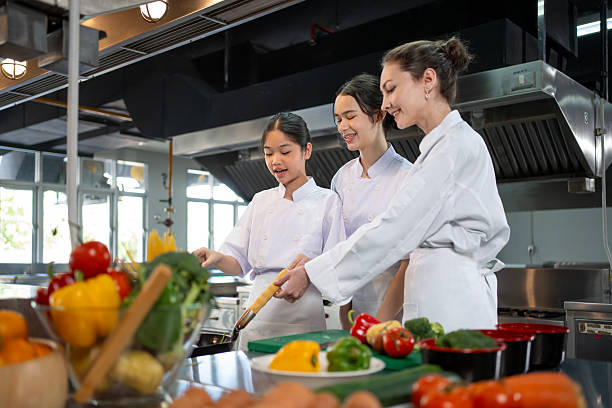 istock Professional chef is teaching young culinary class student to prepare fresh ingredient for the meal inside the restaurant kitchen for fine dining gourmet and cooking school concept 2223147426