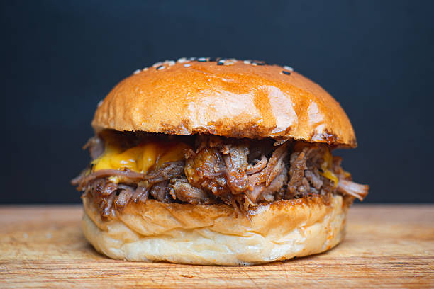 istock Pulled pork hamburger with melted cheddar cheese in sesame seed bun on wooden table close-up. 2223151166