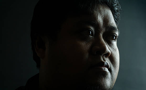 istock Bearded Indonesian man on black background, neutral expression in low-key lighting, simple portrait focusing on natural texture and masculine features 2223155145